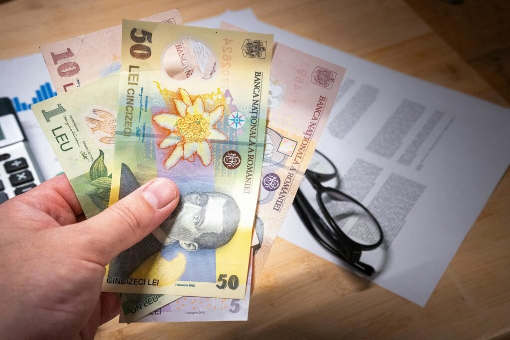 Hand holding Romanian leu banknotes above financial documents, depicting finance and economy.