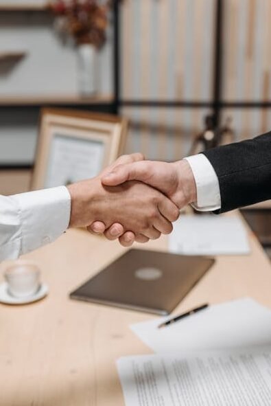 Close-up of two people shaking hands in an office, symbolizing agreement and partnership.